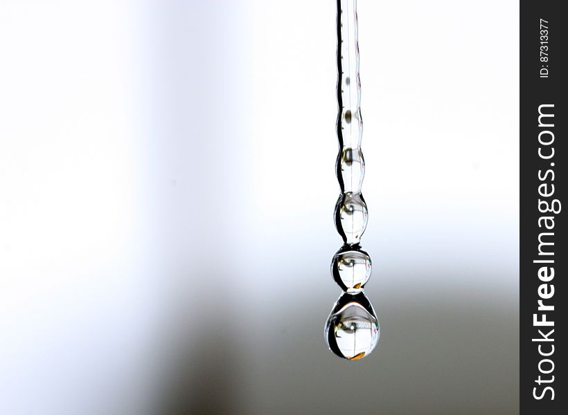 Some water drops hanging from the kitchen faucet, reflecting some parts of the kitchen.