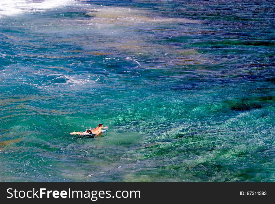 A surfer paddles out to catch some waves in a remote cove on Kauai, Hawaii. The myriad of colors in the water reflect the shallow coral reef that rises up out of the deeper blue water. Learn more about Pacific coral reefs at coralreefs.wr.usgs.gov/ Photographer: Susan Hazlett, USGS