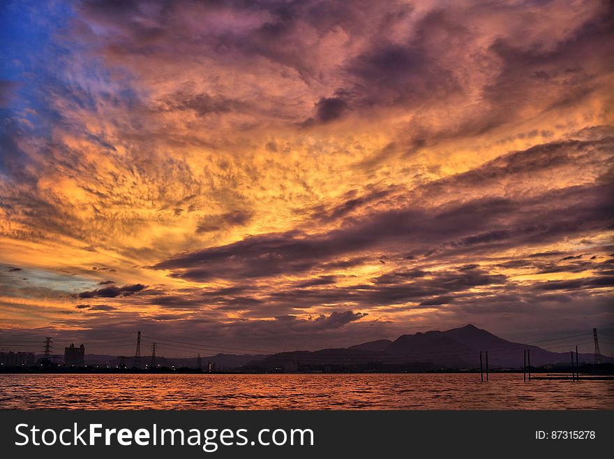 Sea and Silhouette of Mountain Under Orange Sky during Golden Hour
