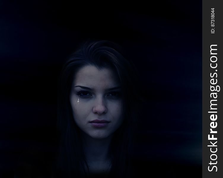 Portrait of crying young woman in shadows with tear rolling down face.