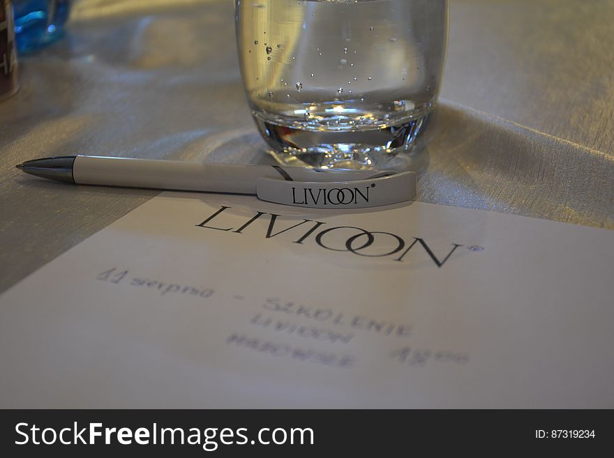 A close up of paper sheet and pen with company logo and a glass of water on a table. A close up of paper sheet and pen with company logo and a glass of water on a table.