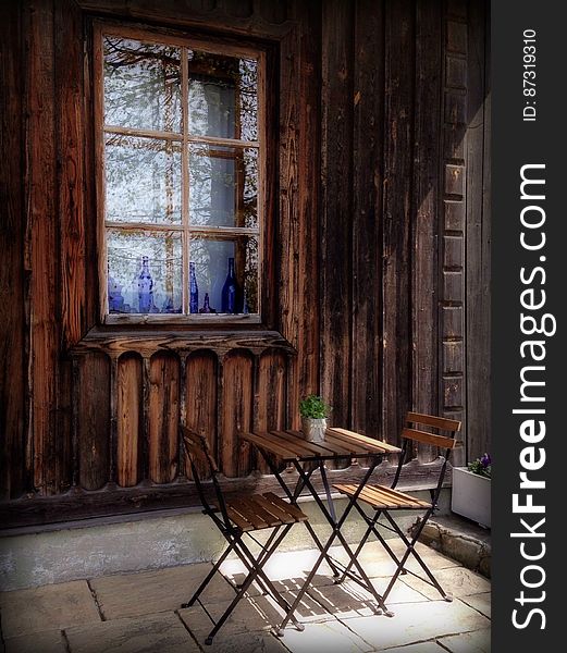 A pair of chairs and a table next to an old wooden house. A pair of chairs and a table next to an old wooden house.