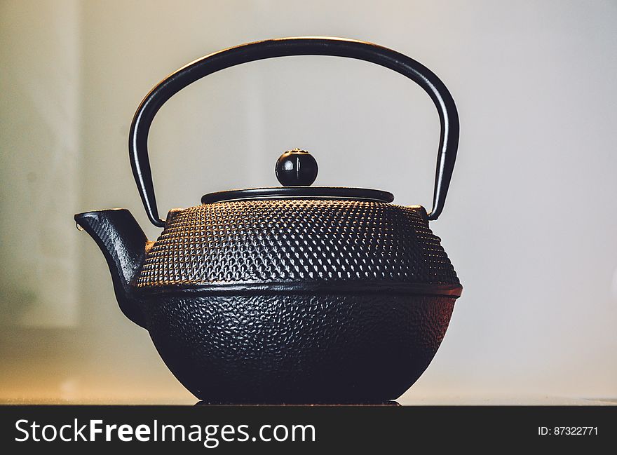 Side view of antique teapot with white wall in background.