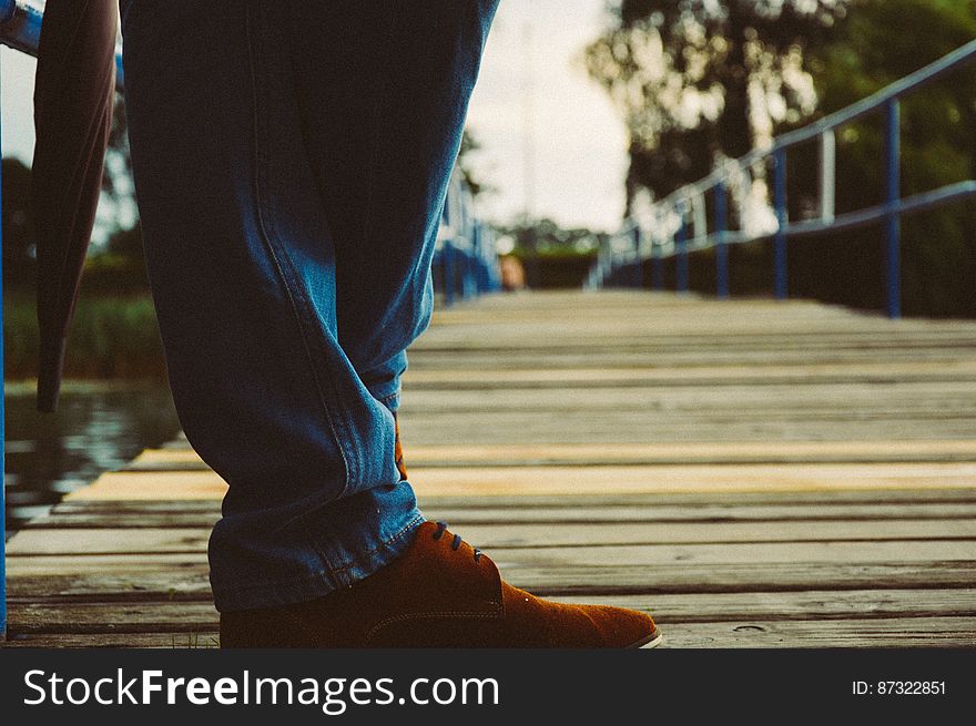 A person with blue jeans and brown shoes standing on wooden pier. A person with blue jeans and brown shoes standing on wooden pier.