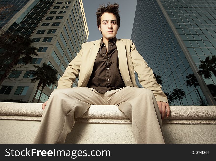 Young businessman sitting on a ledge by buildings