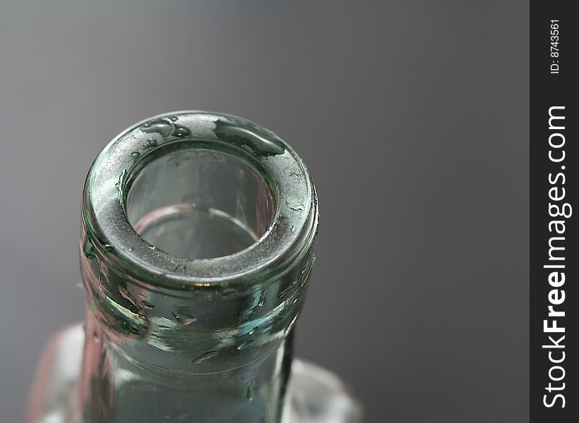 The rim of a bottle with drops of water, shown against a gray background. The rim of a bottle with drops of water, shown against a gray background.