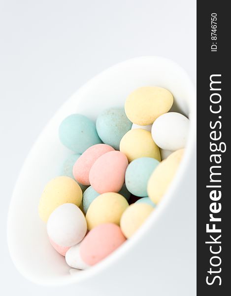 Pastel colored egg shaped candies in white bowl, on white background. There are pink, yellow, green, blue and white ones. Pastel colored egg shaped candies in white bowl, on white background. There are pink, yellow, green, blue and white ones.