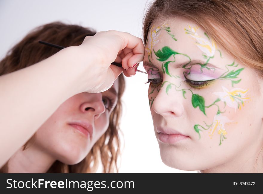 An artist drawing a colorfull flower with green white and yellow on the face of her model. An artist drawing a colorfull flower with green white and yellow on the face of her model