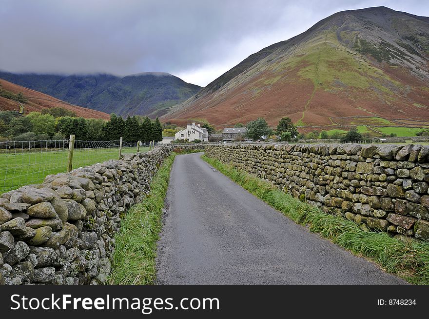 Road leading to Wasdale Head Inn with dry stone walls and mountains with mist on the fells. Road leading to Wasdale Head Inn with dry stone walls and mountains with mist on the fells