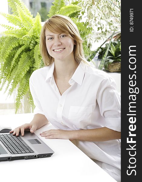 Portrait of young woman in white shirt sitting at the table with plants near by