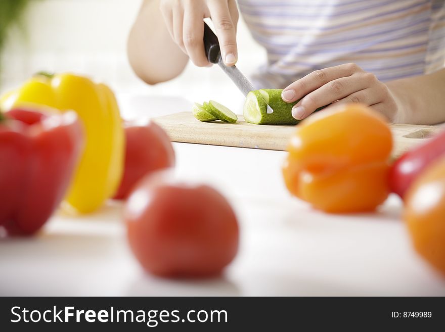 Image of woman cutting cucumber with peppers and tomatoes in front