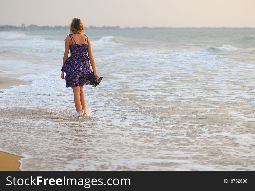 Beautiful young blond girl walking in the water on the beach. Beautiful young blond girl walking in the water on the beach