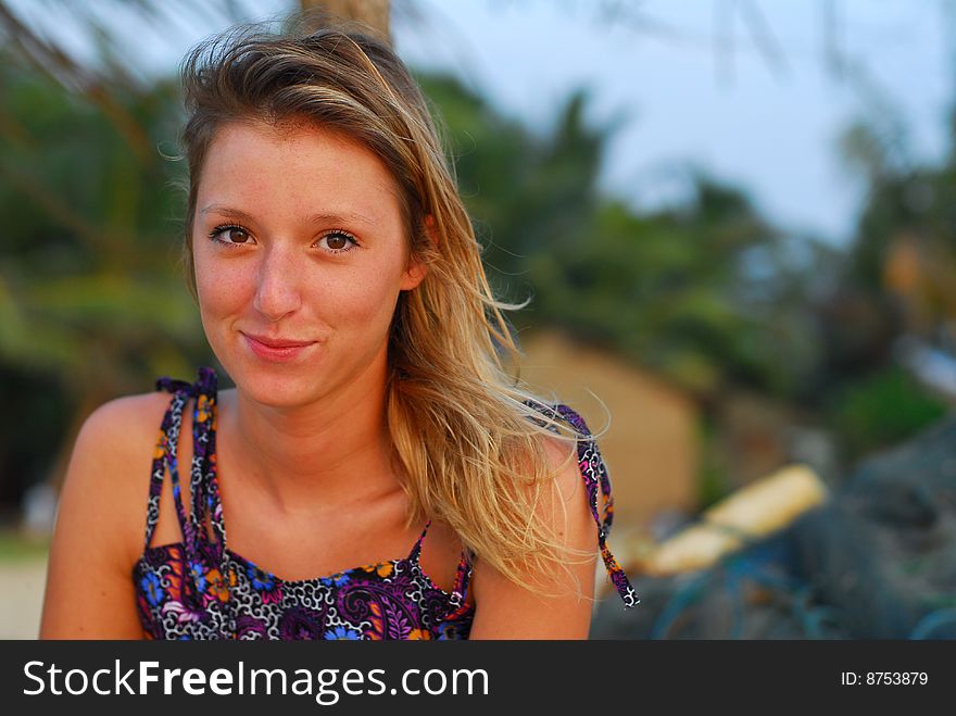 Beautiful, smiling young blond girl sitting on tropical beach with fishing nets in background. Beautiful, smiling young blond girl sitting on tropical beach with fishing nets in background.