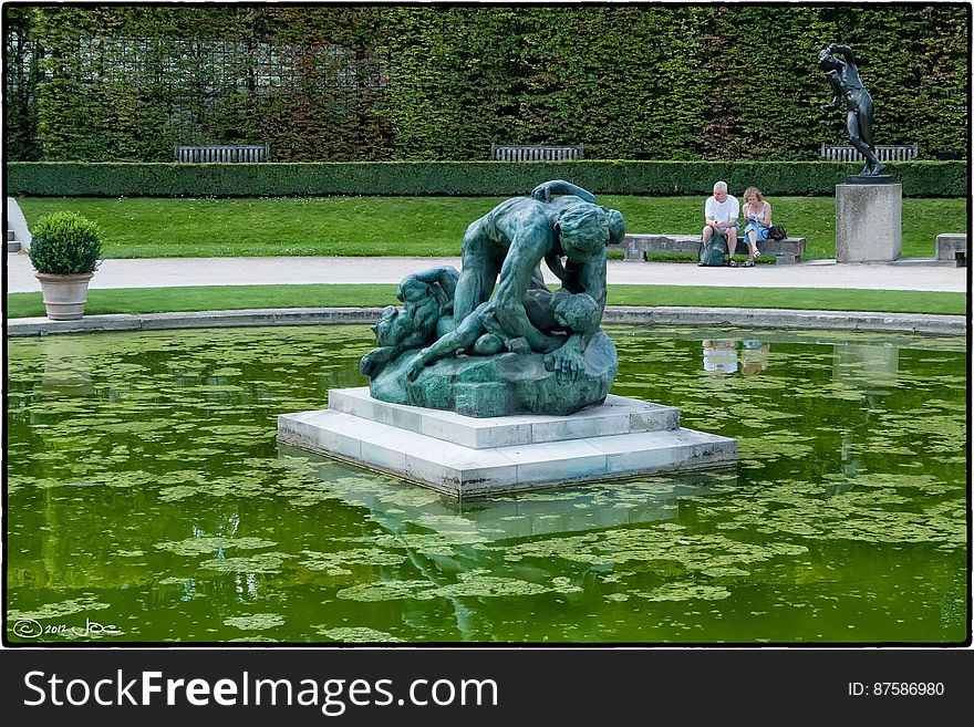 Tourists taking a break near the pond in the garden of the Rodin Museum in Paris. The central statue is &#x22;Ugolino and his children&#x22; and was created circa 1881. Driven crazy by hunger, Ugolino, Count of Gheradesca, devoured his dead children, a crime for which he was eternally damned.