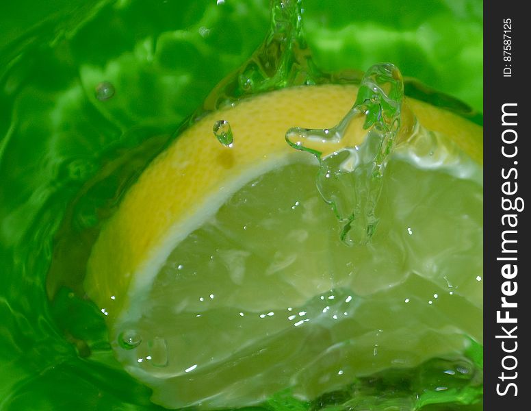 Slice of lemon making splash in water bowl