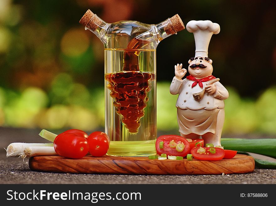 Chef Figurine Beside Clear Glass Bottle and Tomatoes