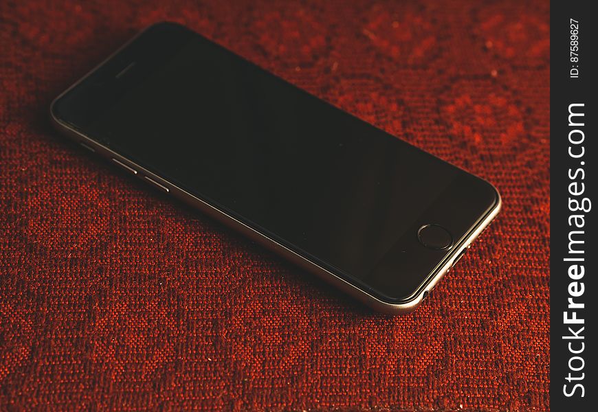 Mobile phone shown with black blank screen, chrome case, charger socket and volume control button, red woven background. Mobile phone shown with black blank screen, chrome case, charger socket and volume control button, red woven background.