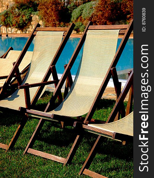 A good close up of some deck chairs behind a pool in a country house