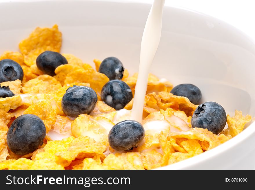 Horizontal view of pouring white milk into a bowl of breakfast flakes with blueberries