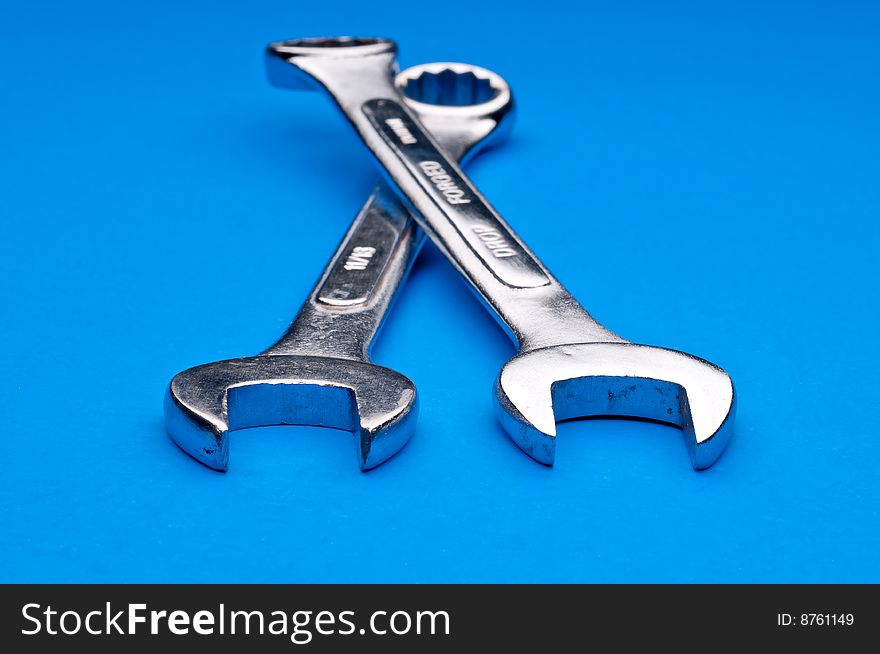 Horizontal image of a pair of old worn combination wrenches on a blue background