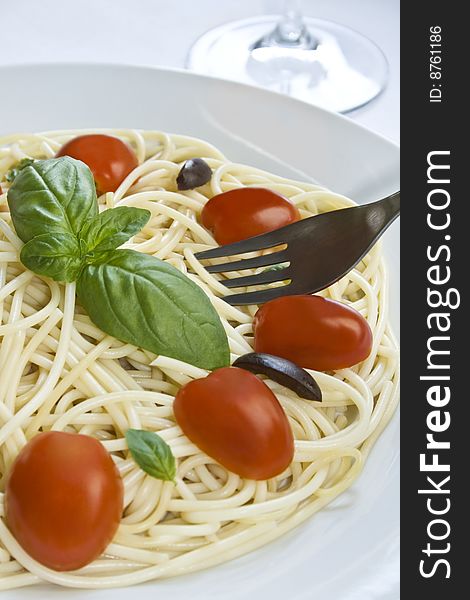 A white dish with spaghetti, cherry tomato, black olives and basil. Focus around basil. A white dish with spaghetti, cherry tomato, black olives and basil. Focus around basil.