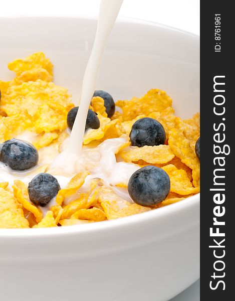 Vertical view of pouring white milk into a bowl of breakfast flakes with blueberries