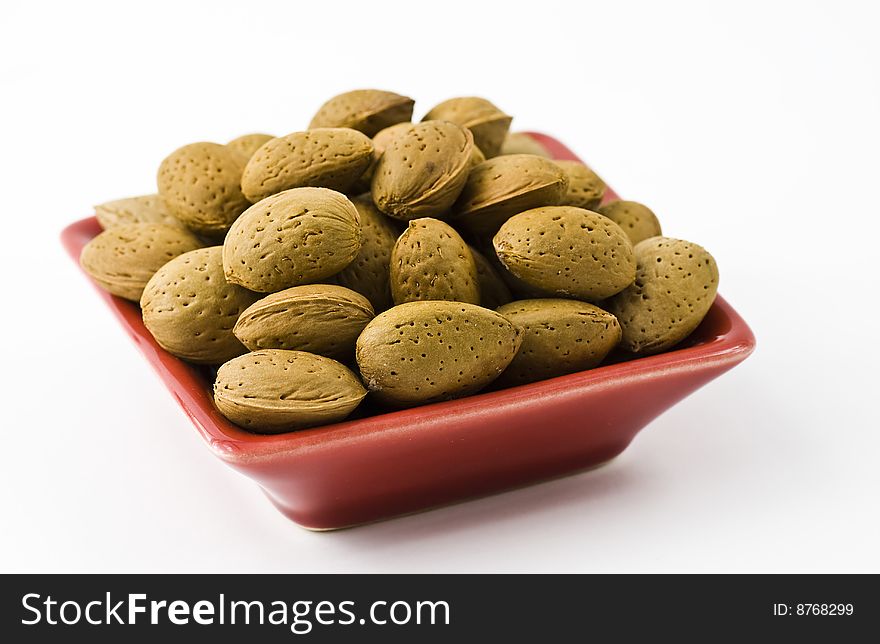 Handful of almonds in the red saucer isolated on the white background