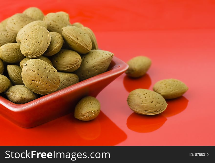 Handful of almonds in the red saucer isolated on the red background and some scattered
