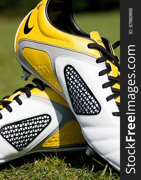 Side view of pair of yellow and white football boots on grass.