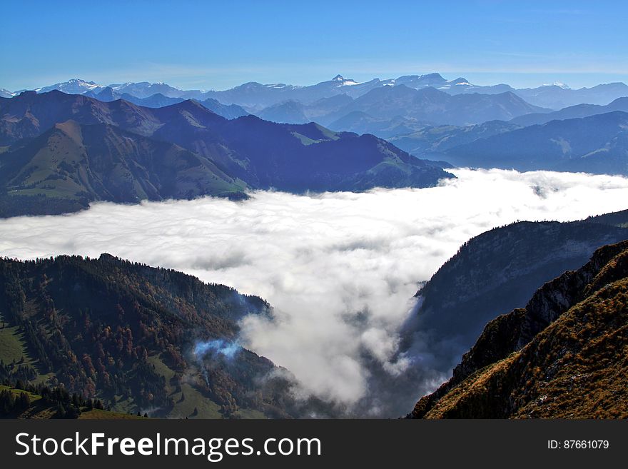 Aerial view over mountain peaks with fog in valley on sunny day with blue skies. Aerial view over mountain peaks with fog in valley on sunny day with blue skies.