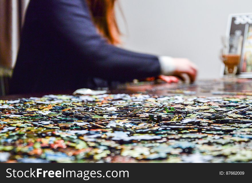 Woman with red hair and blue jacket doing a jigsaw puzzle on a table with selective focus on a few of the unplaced pieces. Woman with red hair and blue jacket doing a jigsaw puzzle on a table with selective focus on a few of the unplaced pieces.