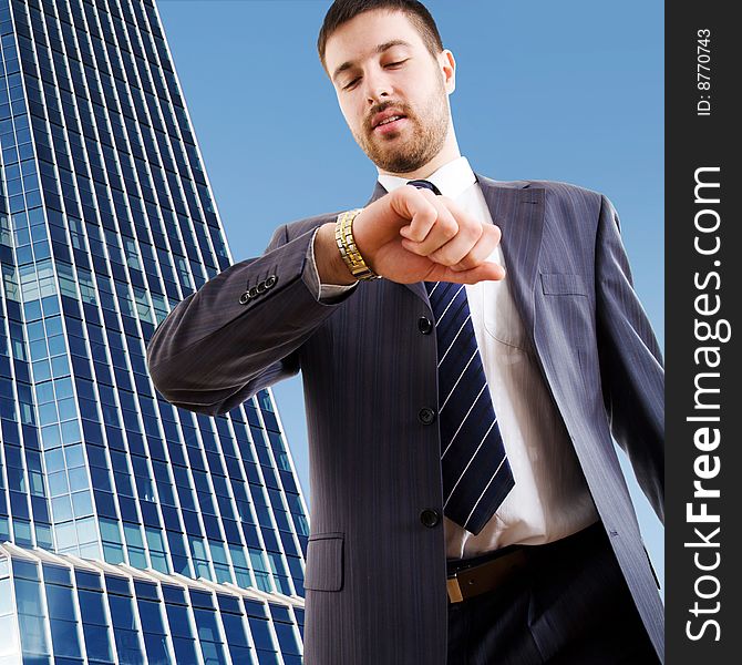 The modern businessman looking at wrist watch against a skyscraper