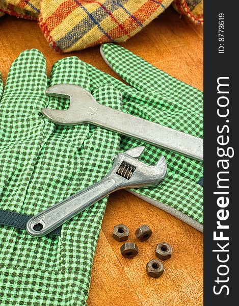 Spanners and nuts laying on gloves on wooden table.