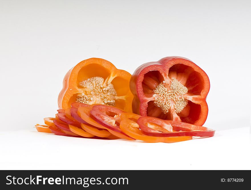 Cut orange and red sweet pepper showing seeds with slices on white. Cut orange and red sweet pepper showing seeds with slices on white