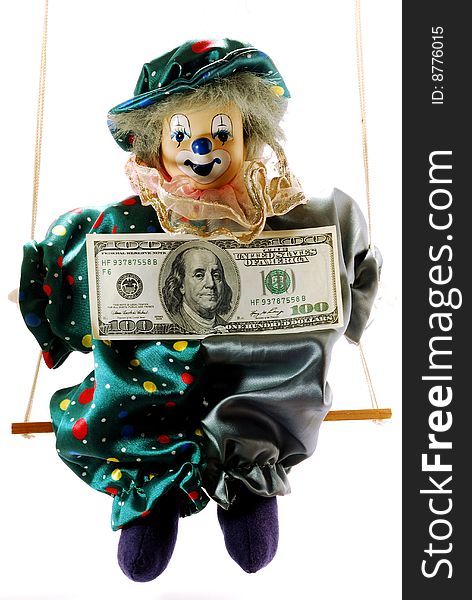 The cheerful clown sits on a swing with dollar on a stomach. The cheerful clown sits on a swing with dollar on a stomach