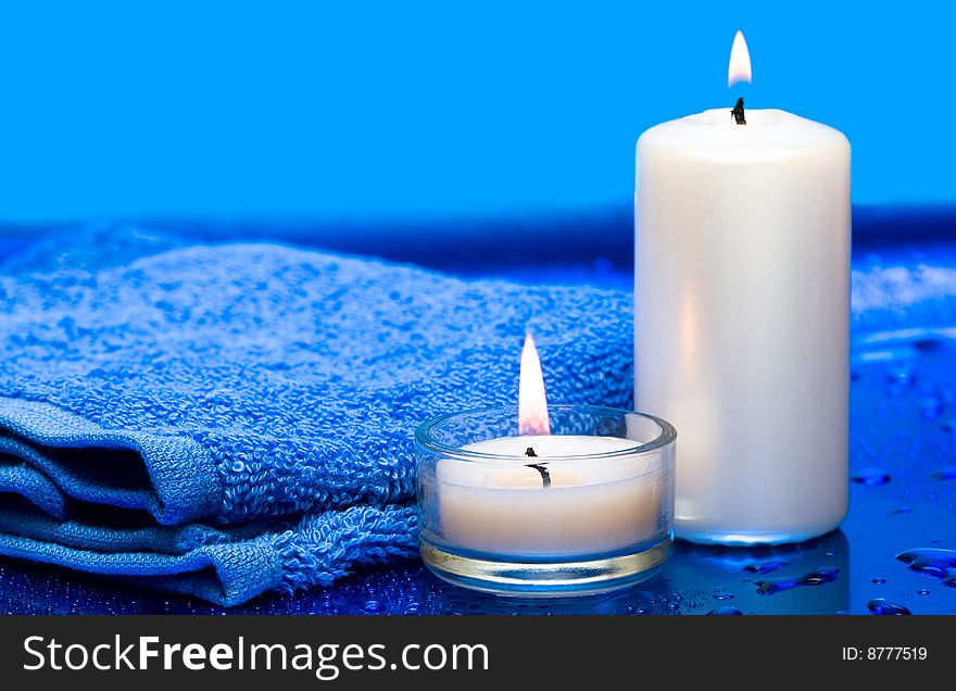 Spa essentials, candles and towel on blue background