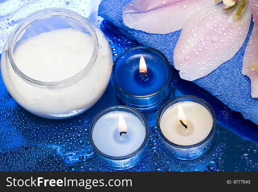 Spa essentials, cream, candles with flower on blue background