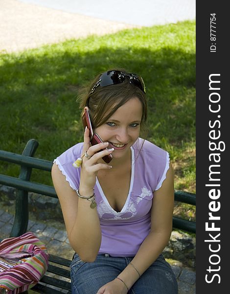 A nice blonde girl sits on a bench in the park chatting on the mobile phone. A nice blonde girl sits on a bench in the park chatting on the mobile phone