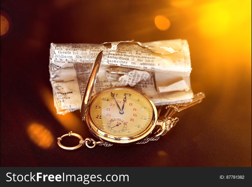 Close up of vintage pocket watch with old paper against bokeh gold lights.