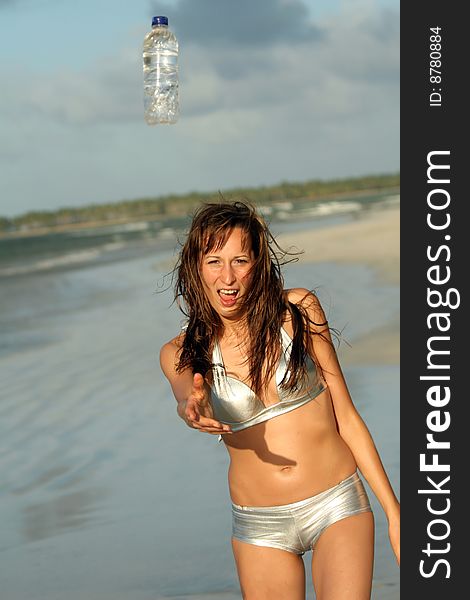 Woman in silver bikinis on the beach throwing bottle water. Woman in silver bikinis on the beach throwing bottle water