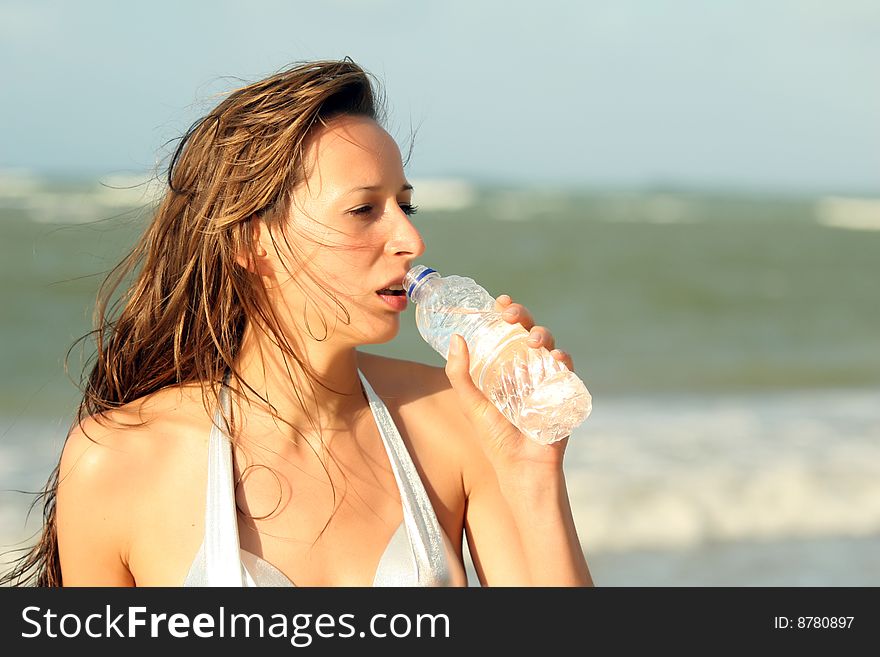 Woman drinking water on the beach by sunset