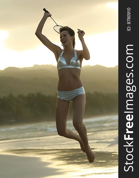 Woman playing badminton on the beach by sunset