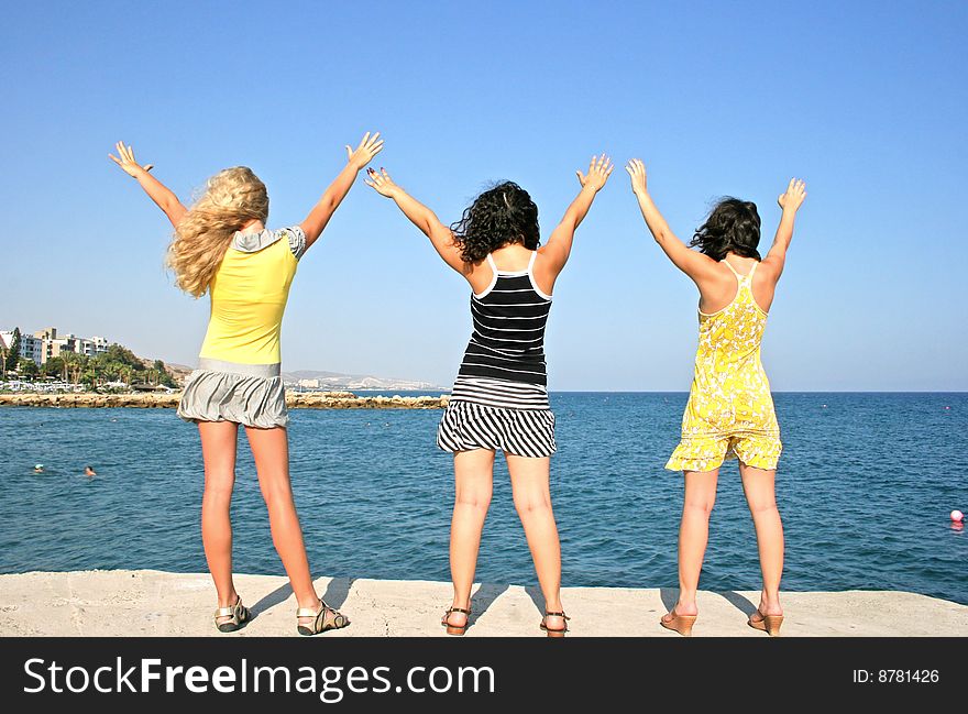 Three pretty girls hands up at the sea.