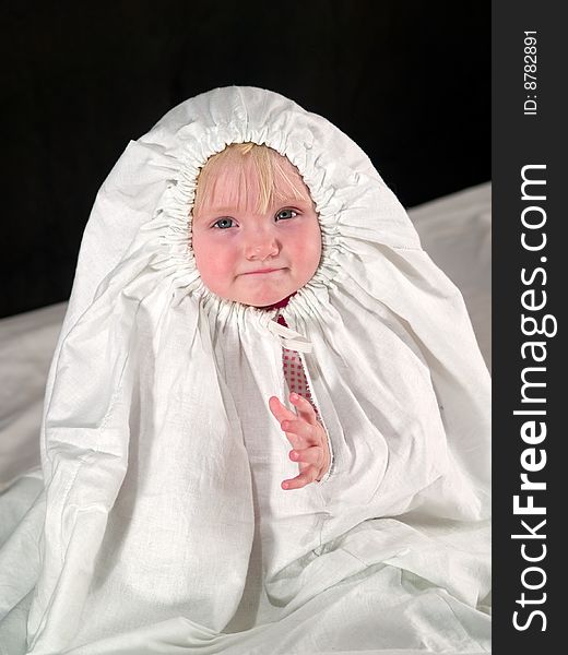 Child sits in white cloth and looking into camera