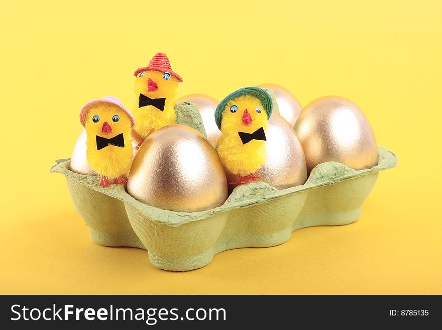 Golden Easter eggs and chicks in carton over yellow background