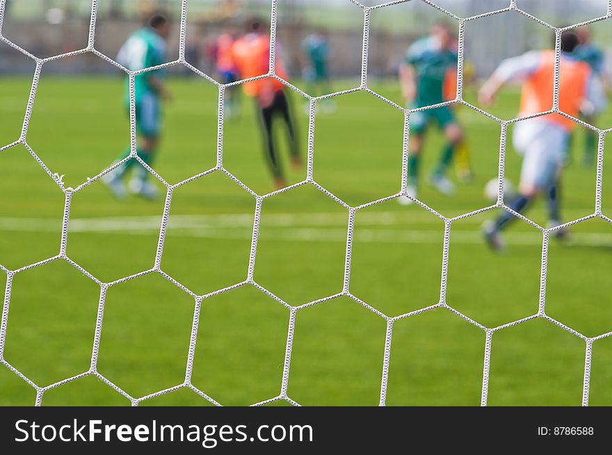 Football ground and football players through a grid of gate - an abstract dim background. Football ground and football players through a grid of gate - an abstract dim background.