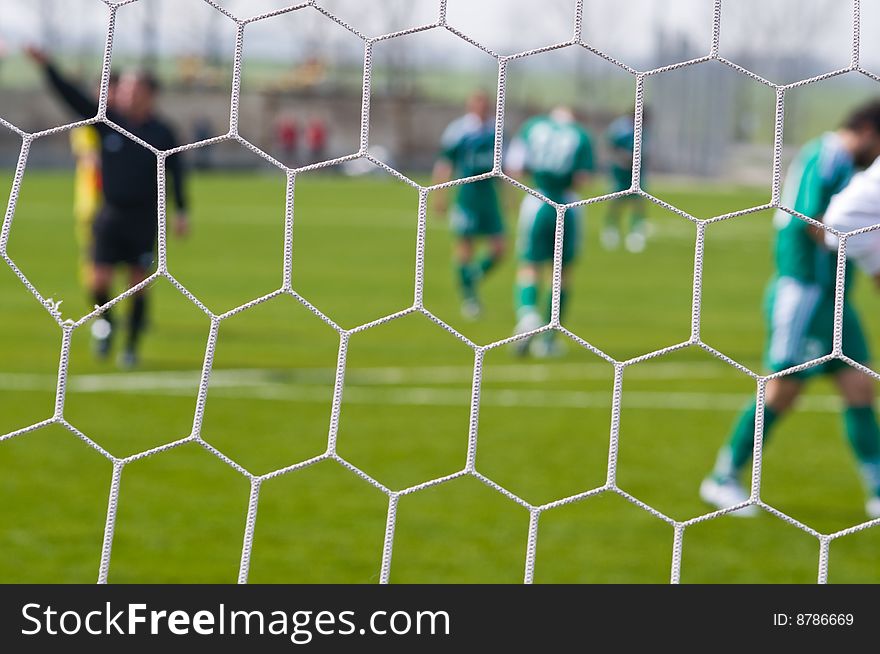 Football ground and football players through a grid of gate - an abstract dim background. Football ground and football players through a grid of gate - an abstract dim background.