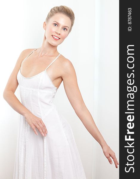 Portrait of a caucasian blonde Ballerina dancer dressed in white striking ballet pose.