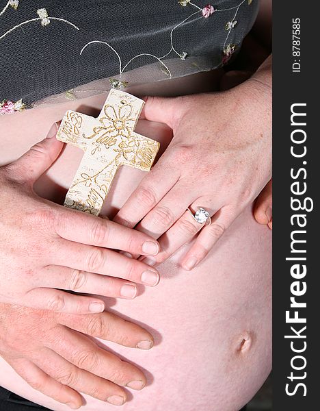 Heavily pregnant couple holding a cross on tummy. Heavily pregnant couple holding a cross on tummy