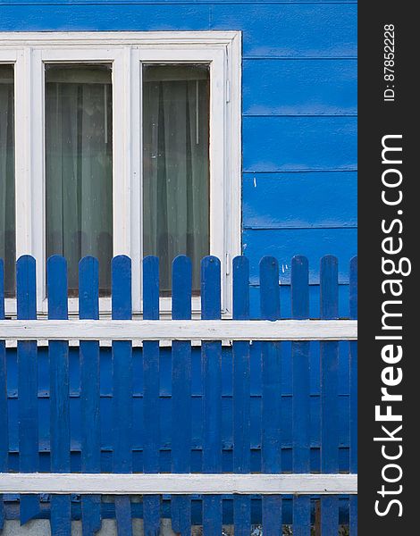 Country Home Painted In Blue, With White Window Frames And Matching Fence.